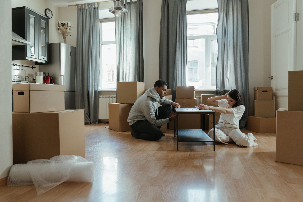 services-01 Young couple putting together furniture in their new apartment, with cardboard boxes all around.